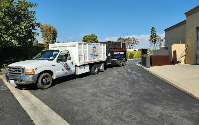 White work pickup with a stake body towing a dump trailer on a small business lot
